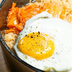 Close-up of a savory ramen bowl topped with a fried egg and spicy kimchi, showcasing vibrant culinary colors.