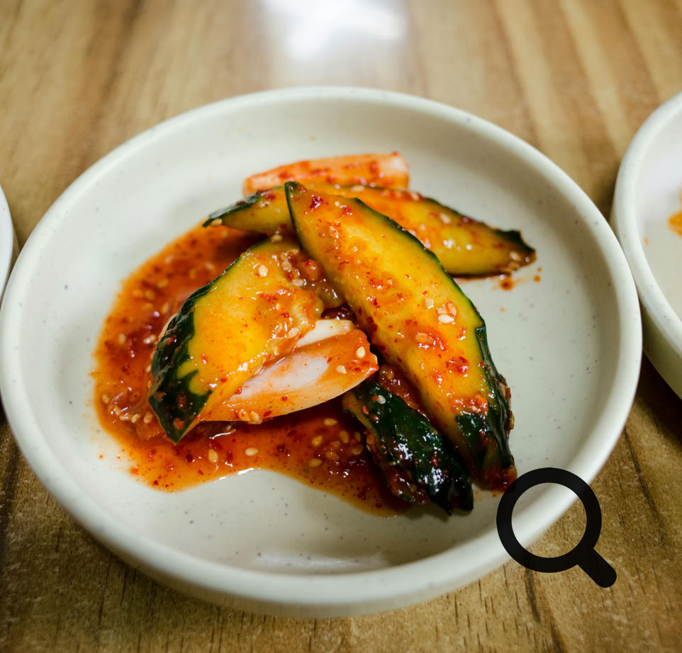 A close-up of spicy Korean cucumber kimchi arranged in a white ceramic bowl on a wooden table.