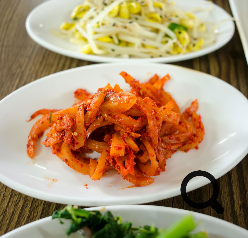 A vibrant collection of Korean side dishes featuring spicy kimchi, fresh greens, and bean sprouts.