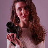 Female photographer in a studio holding a camera with a serious expression.