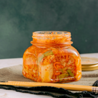Close-up of homemade kimchi in a jar with chopsticks on a table.