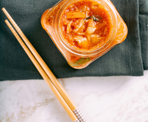 Delicious homemade kimchi in a glass jar with wooden chopsticks on a green napkin.